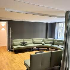 Lounge-Bereich im Satellite Office Ludwigpalais mit grünem, halbkreisförmigem Sofa, integrierten Tischen und dunkler Akzentwand
