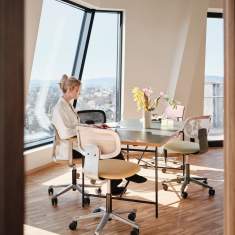 HÅG Tion mesh Bürostühle von Flokk in Beige und Grün in einem hellen Büroraum, Frau arbeitet am Tisch mit Laptop
