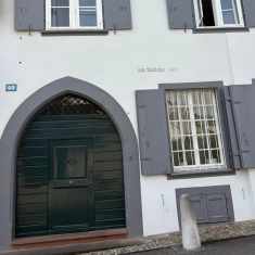 Historischer Gebäudeeingang mit Rundbogentür und Fensterläden in Grau.